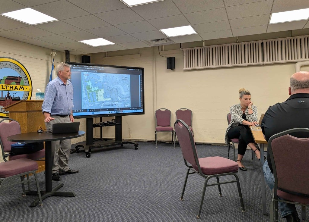 In the City Hall basement meeting room, Jeffery McElravy stands in front of a digital presentation board showing a layout of 155 Lexington St. The existing fire headquarters and emergency services administration buildings are picked out in white, and the proposed future police headquarters and vehicle fueling station are picked out in yellow.
